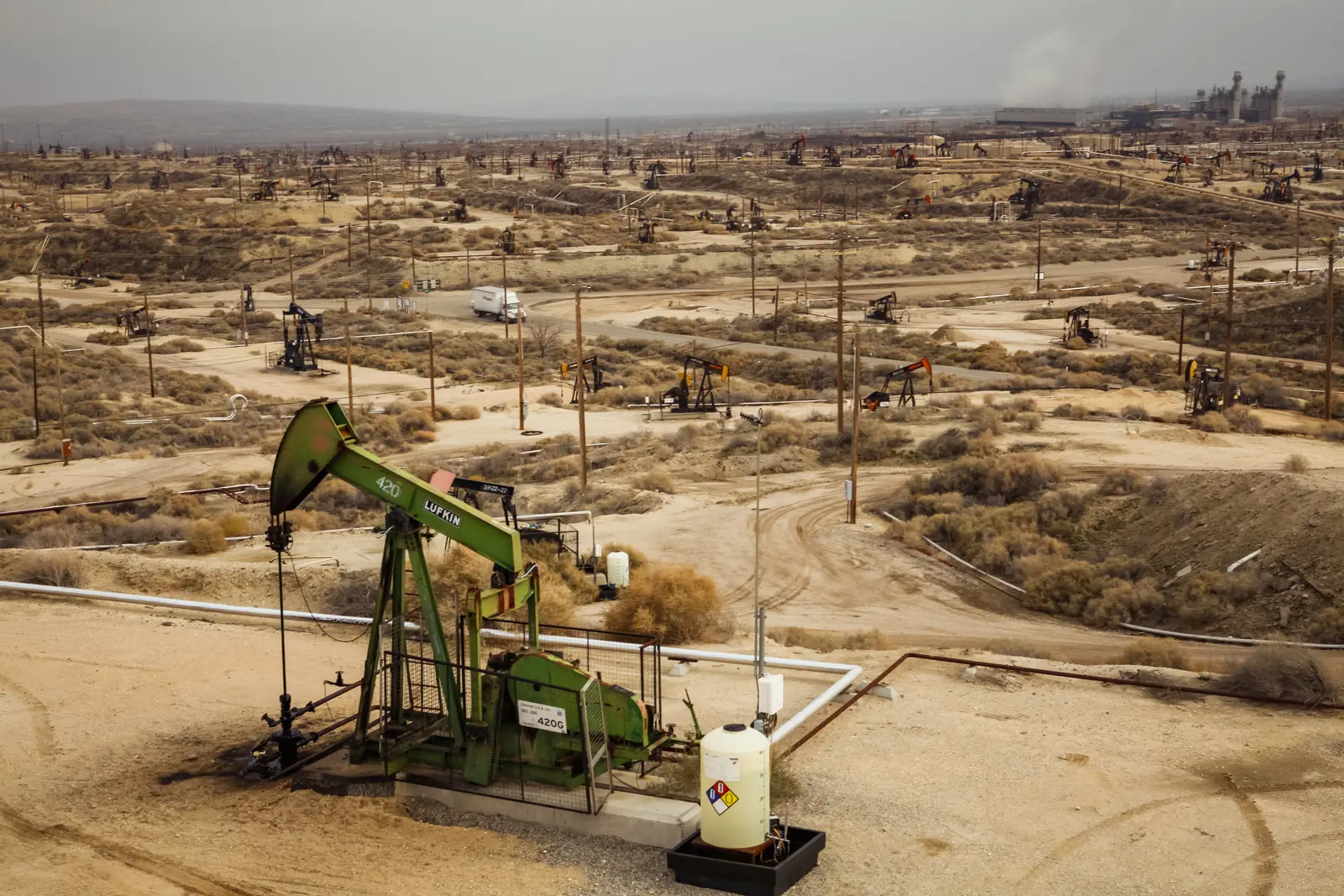 A working oil drilling site in Kern County, California — a pumpjack in the foreground with wells and rigs stretching to the horizon
